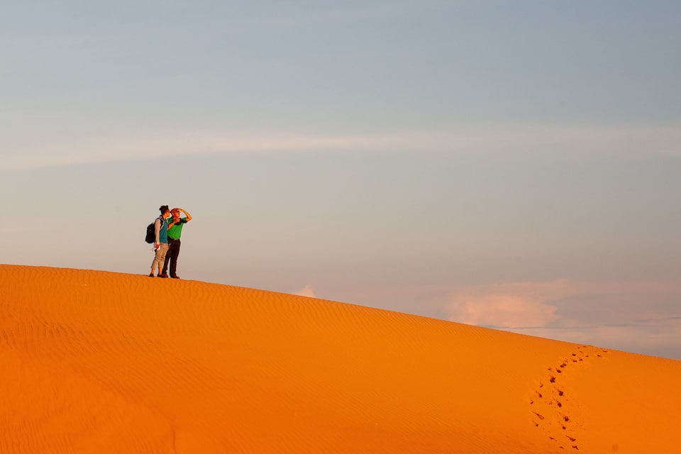 Two people standing on a sand dune with a clear sky in the background.