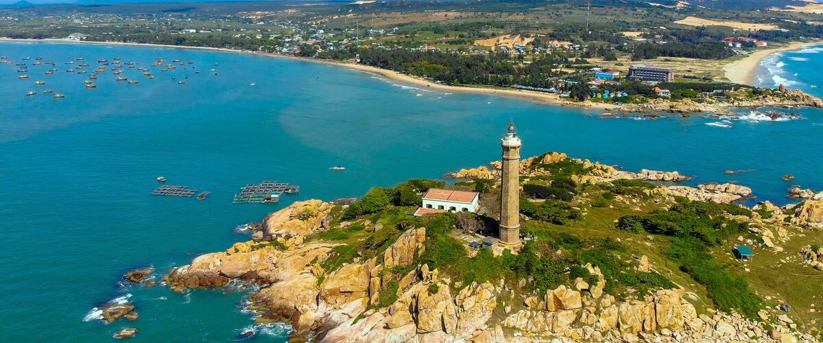 A coastal town with a lighthouse, rocky coastline, and a mountain in the background.
