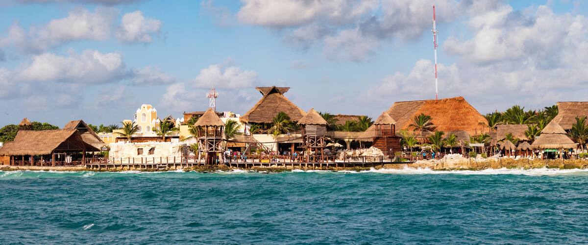 A coastal resort with thatched-roof buildings and palm trees.