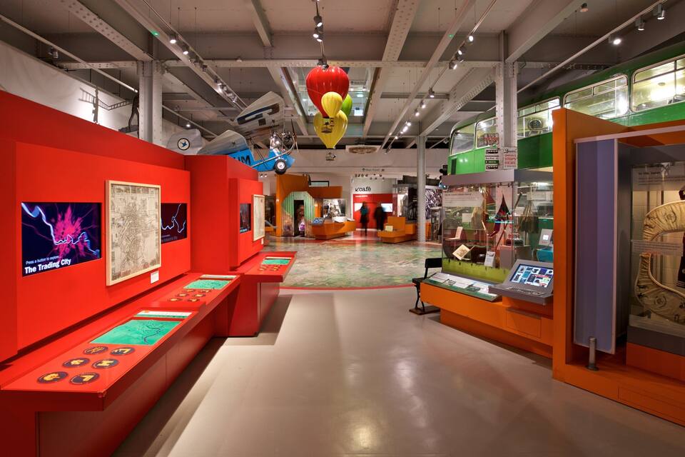An indoor exhibition with red walls, various displays, and a green bus model.