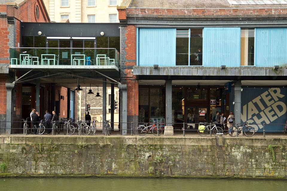 A riverside building with a blue shutter, a water shed sign, and bicycles parked outside.