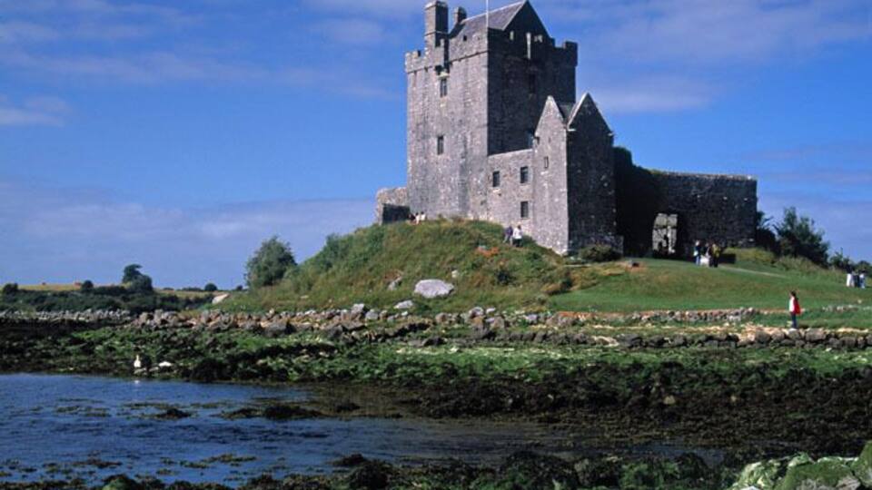 A historic castle on a grassy hill overlooking a body of water.