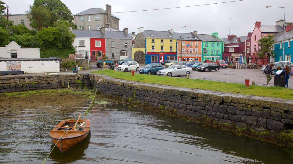 A narrow waterway with a wooden boat, colorful buildings, and parked cars along the shore.