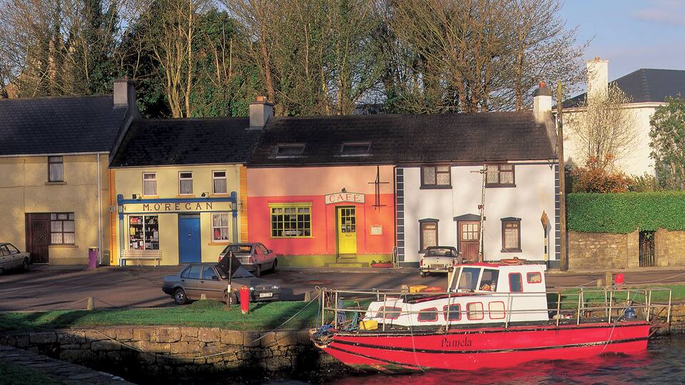A red boat named Pamela docked at a harbor with colorful buildings in the background.