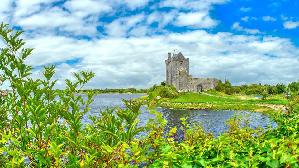 A historic stone tower by a lake surrounded by lush greenery.