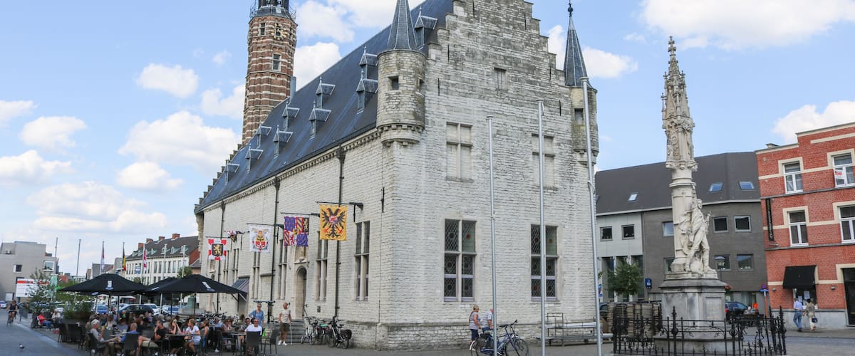 A historic building with a tower, flags, and a statue in a public square.