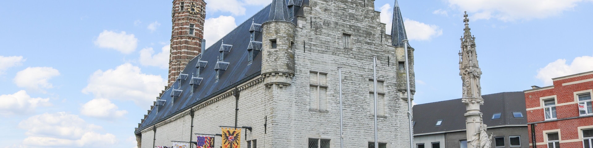 A historic building with a tower, flags, and a statue in a public square.