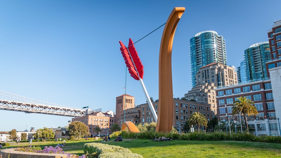 Stadsbeeld met moderne gebouwen, een groot rood sculptuur en een brug.