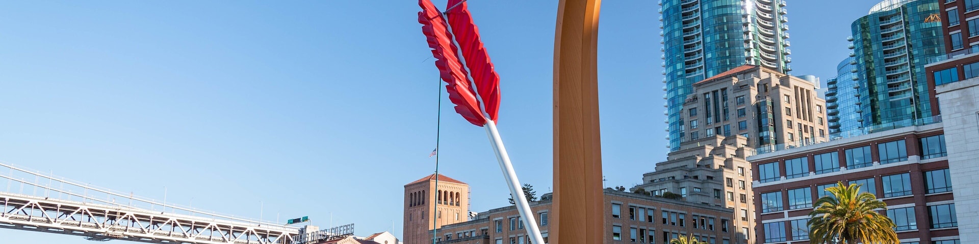 Vista urbana com edifícios modernos, uma grande escultura vermelha e uma ponte.