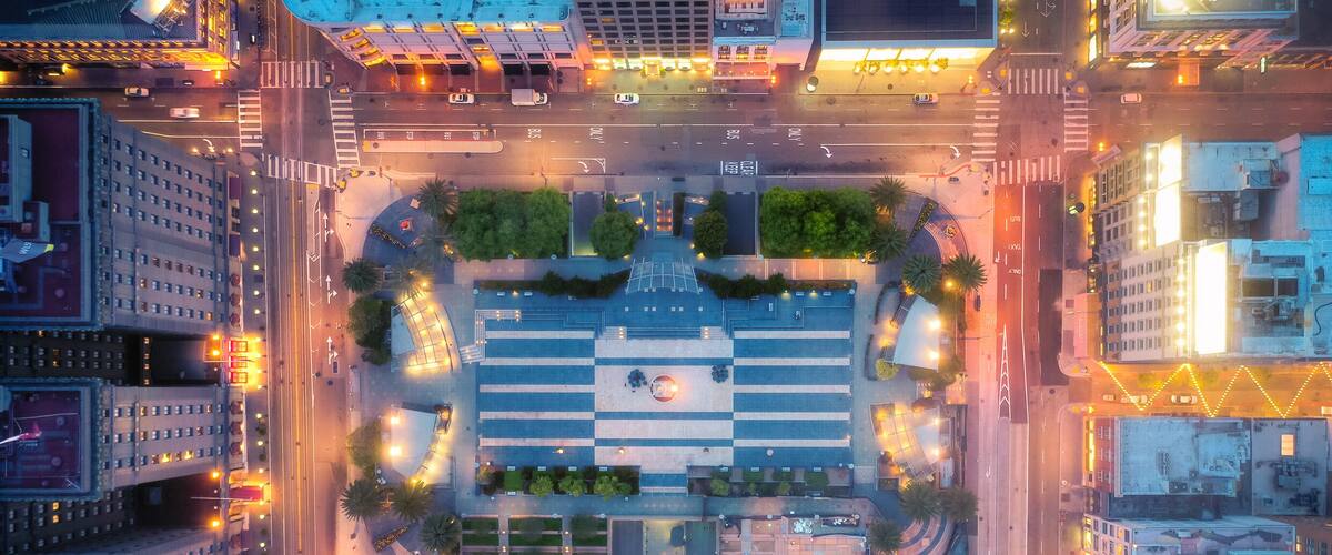 An aerial view of a city intersection with buildings, roads, and a central plaza.