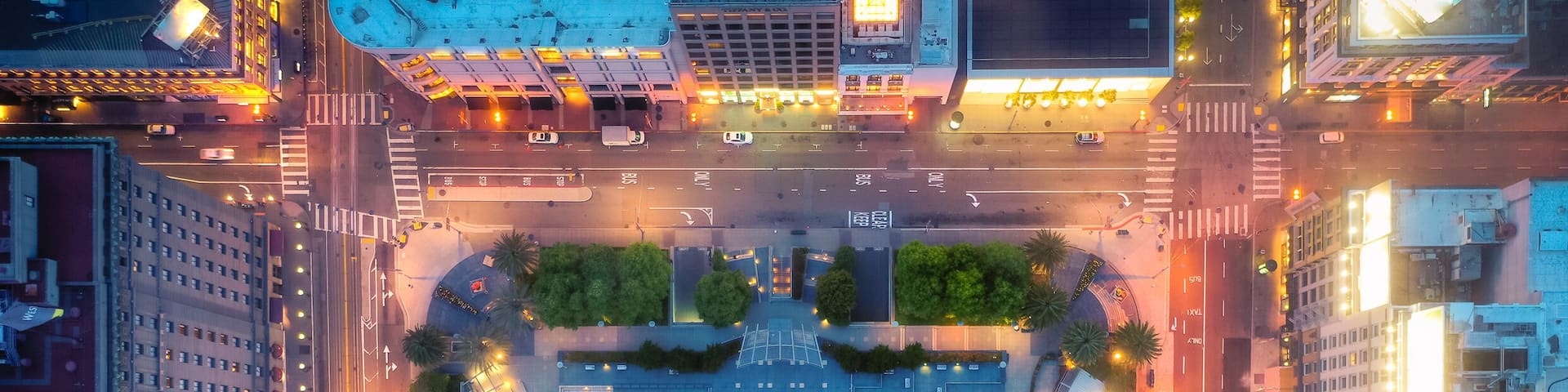 An aerial view of a city intersection with buildings, roads, and a central plaza.