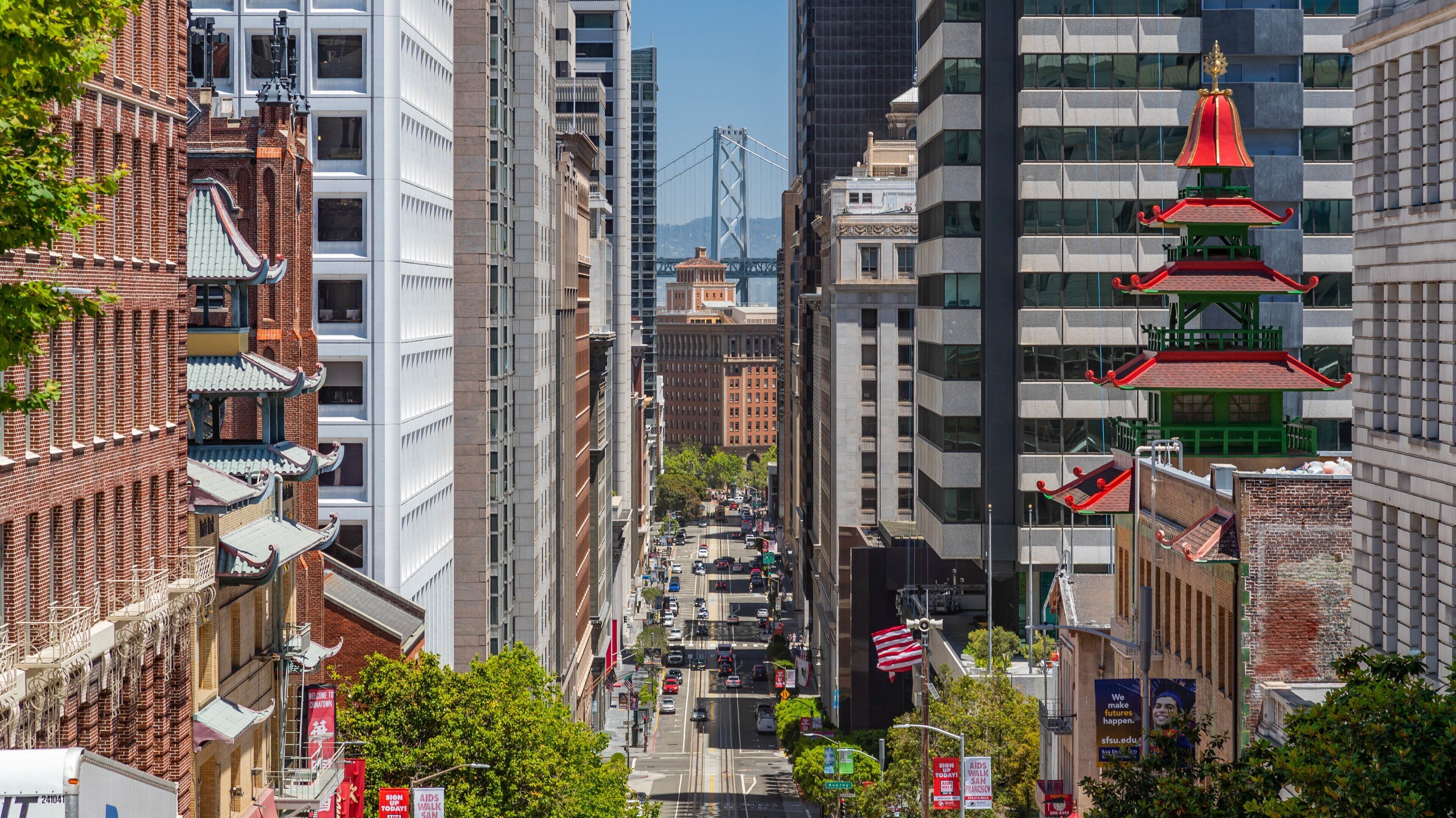 A city street lined with modern and traditional buildings, including a bridge in the background.