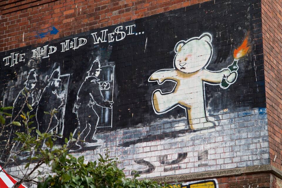 Un mural en una pared de ladrillo con grafitis y un oso sosteniendo una antorcha.