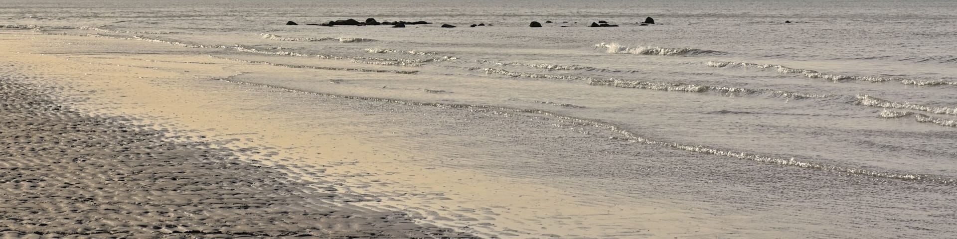 A beach with gentle waves and scattered rocks.
