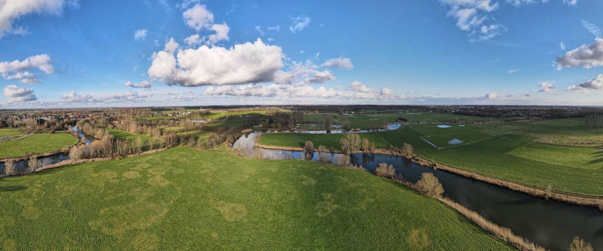 A river meandering through green fields, with a town in the distance and a clear blue sky.