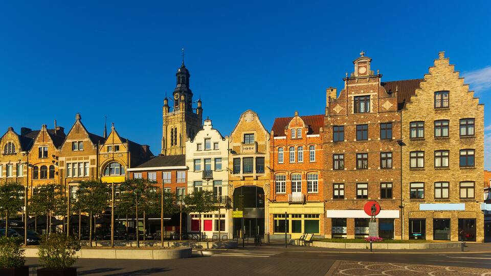 A row of historic buildings with a prominent church tower and a statue in the foreground.