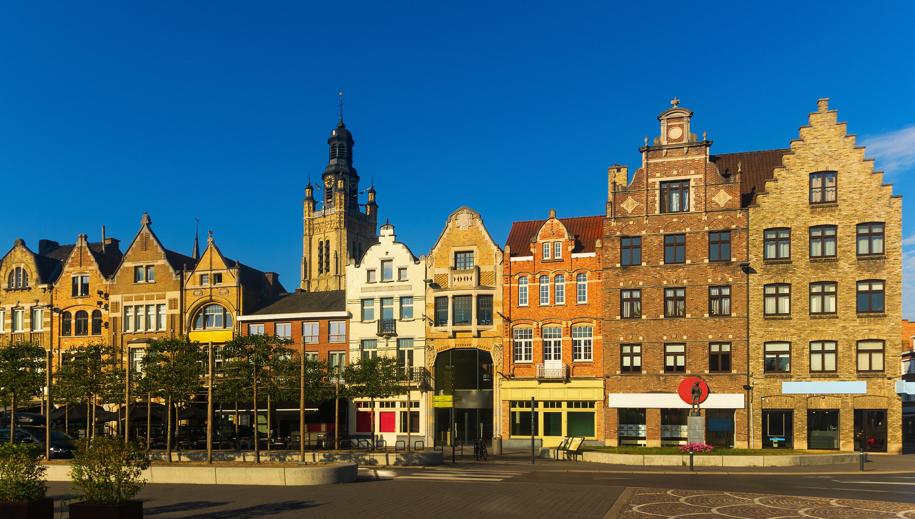 A row of historic buildings with a prominent church tower and a statue in the foreground.