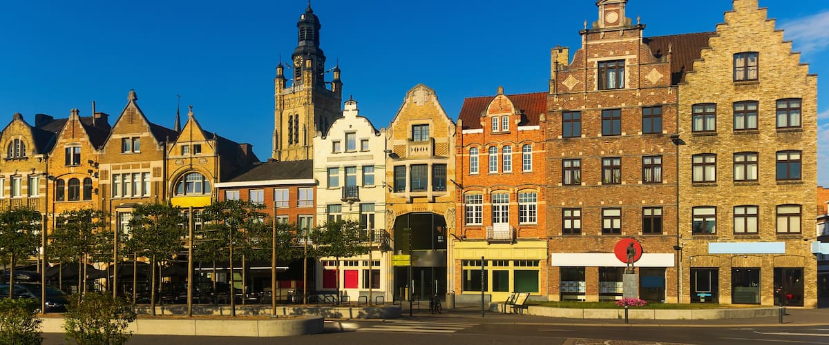 A row of historic buildings with a prominent church tower and a statue in the foreground.