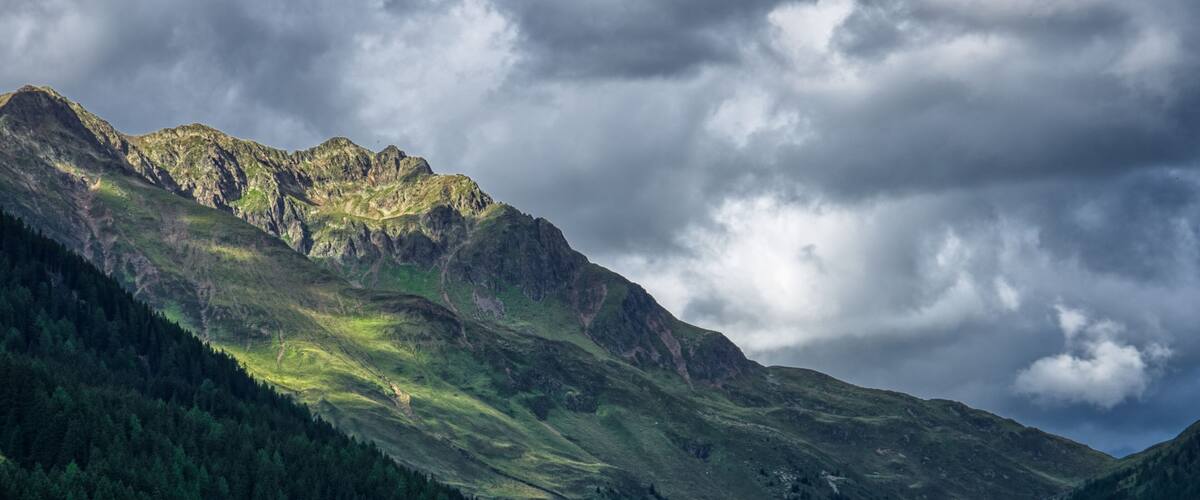 A mountain range with a forested valley and a cloudy sky.