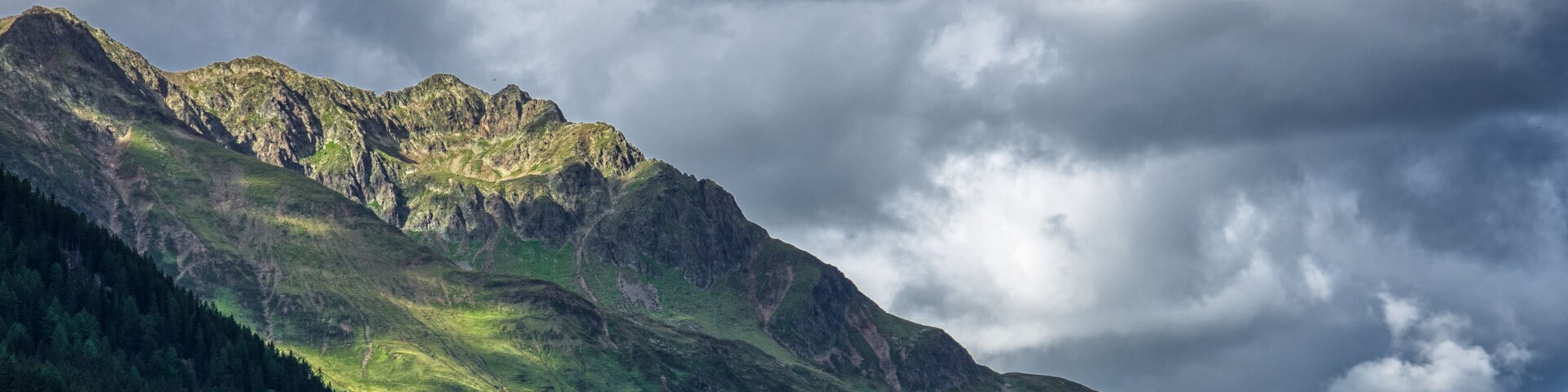 A mountain range with a forested valley and a cloudy sky.