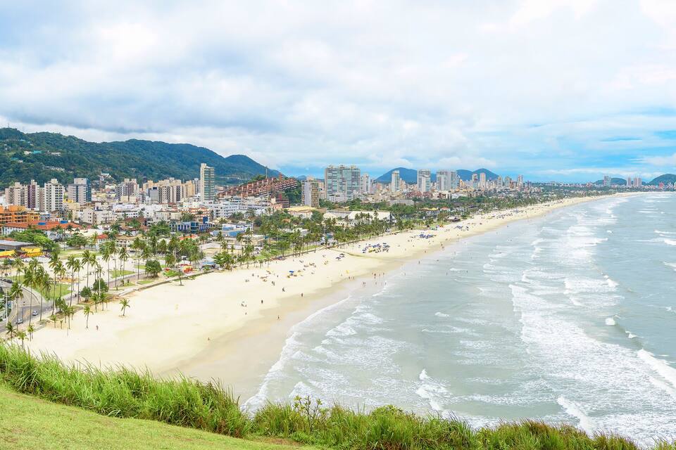 Una ciudad costera con una extensa playa arenosa, edificios altos y montañas al fondo.