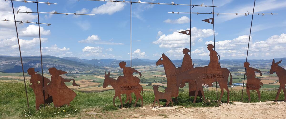 A metal sculpture of figures on horseback in a rural landscape with mountains in the background.