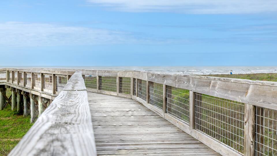 A wooden boardwalk leading to a beach with a metal railing on one side.