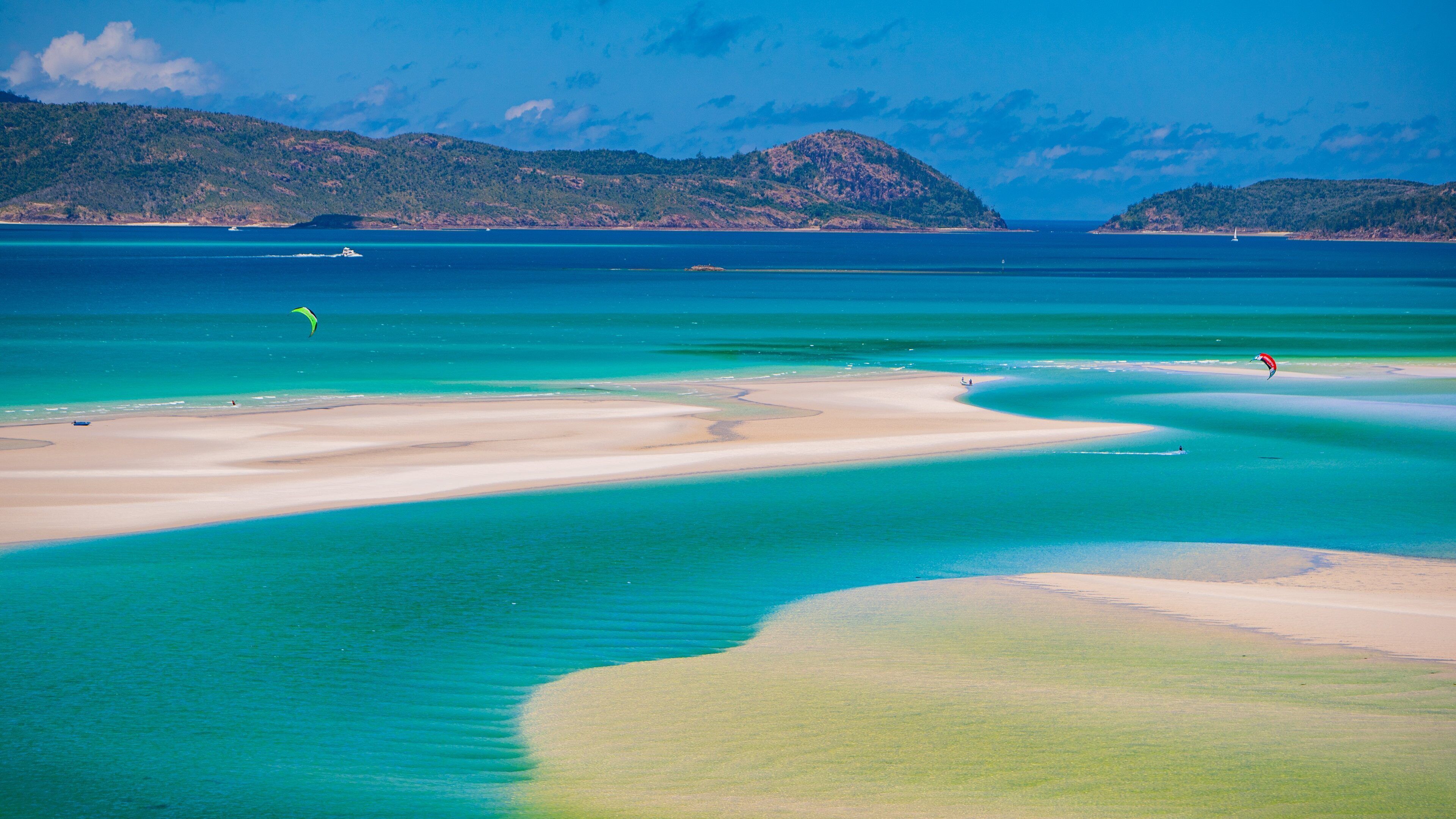 A coastal landscape with clear turquoise waters, sandy beaches, and distant green hills.