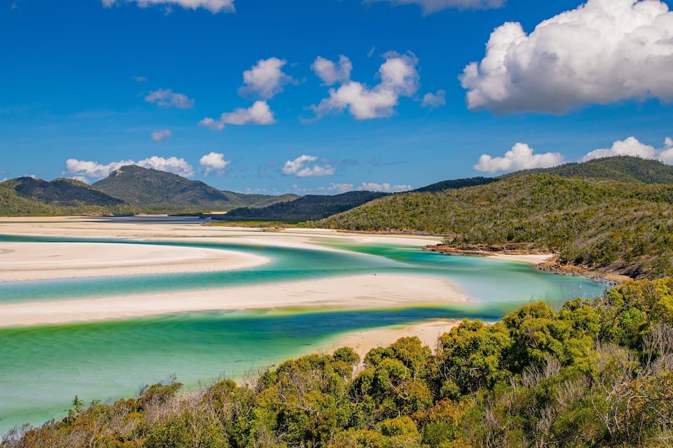 A coastal landscape with clear turquoise waters, sandy beaches, and green hills.