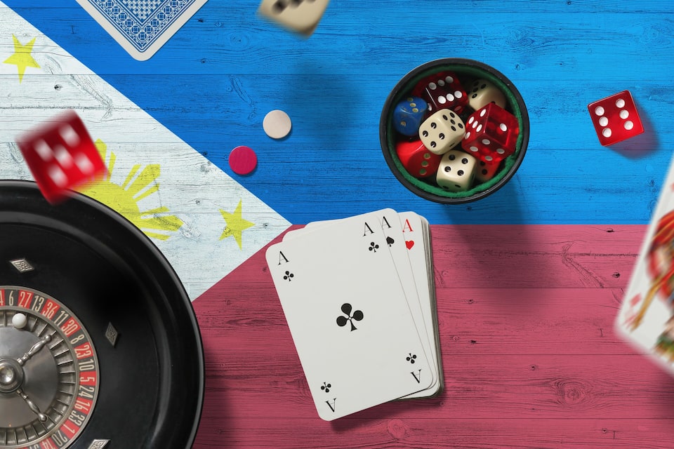 A roulette wheel, playing cards, and dice on a wooden table with a flag design.