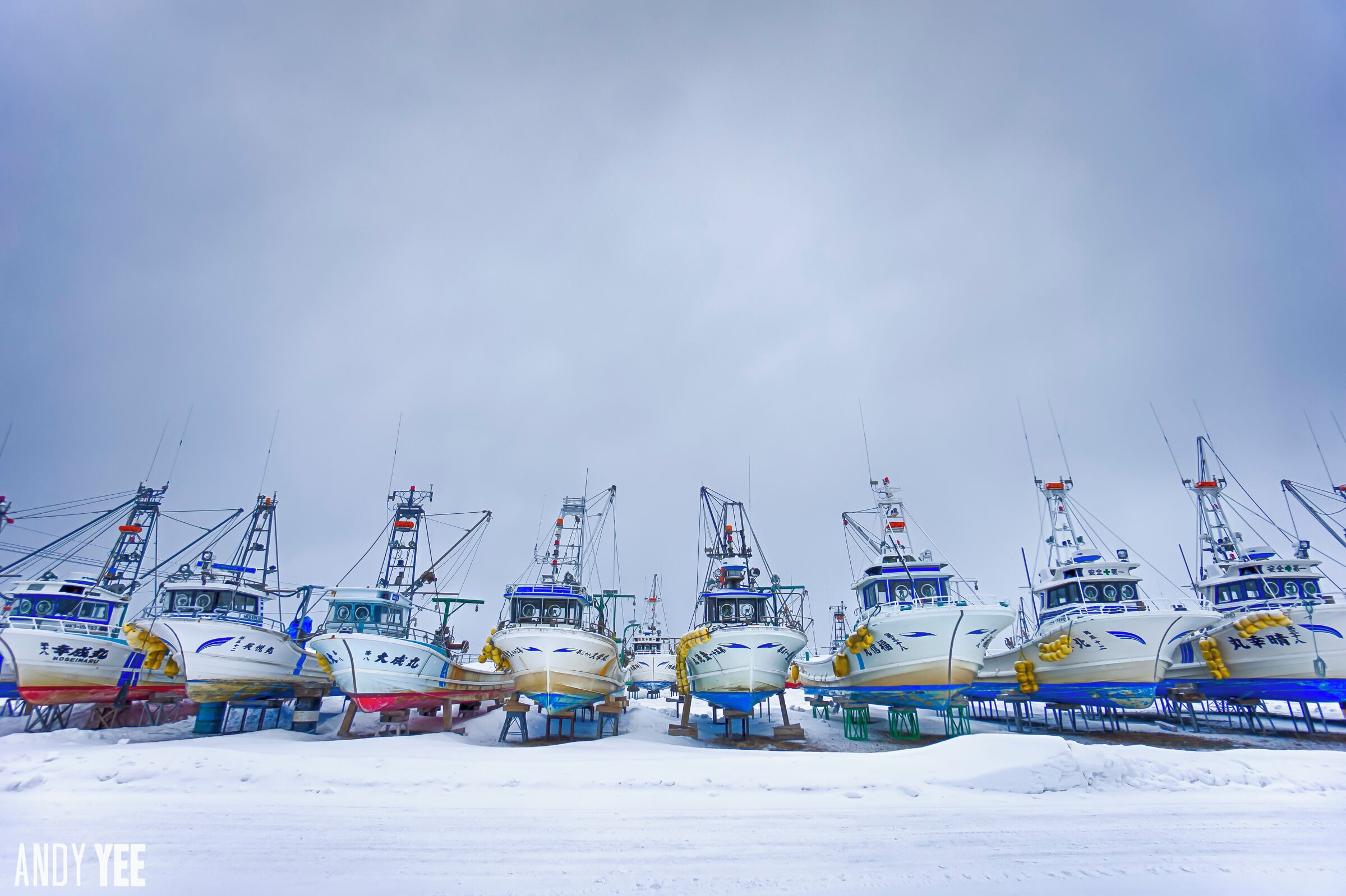 Several fishing boats docked in a snowy harbor.