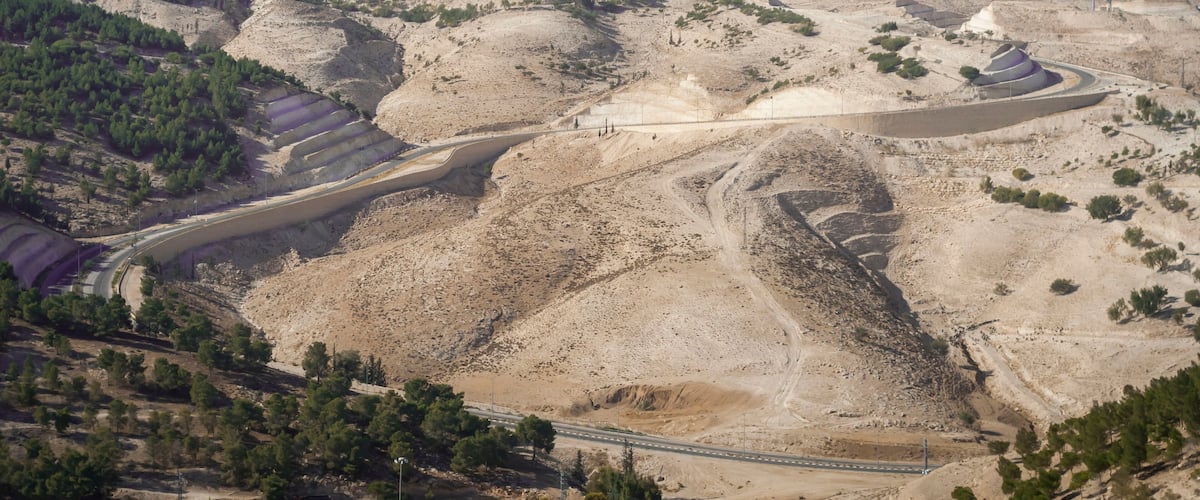 A mountainous landscape with terraced fields, a winding road, and a distant city.