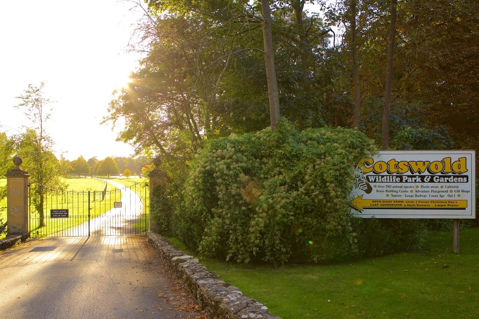 Een bordje voor Cotswold Wildlife Park & Gardens, met een pad door een groen landschap.
