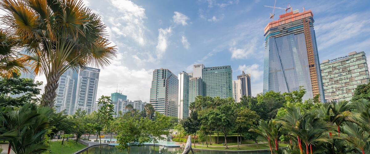 A cityscape with modern skyscrapers, a central pond, and surrounding greenery.
