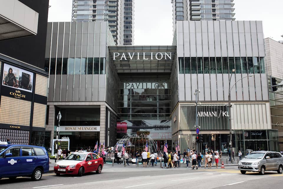 A busy urban street with a prominent building labeled 'Pavilion' and 'Armani / KL' on its facade.