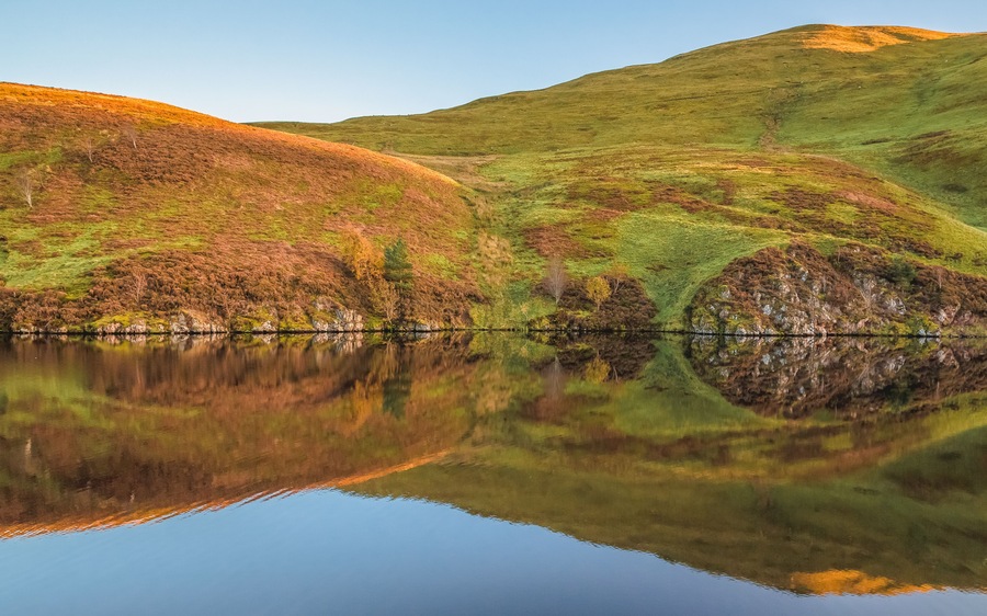 A calm, still peaceful countryside landscape reflection at Glencorse Reservoir in the Pentland Hills Regional Park in Edinburgh, Midlothian, Scotland.