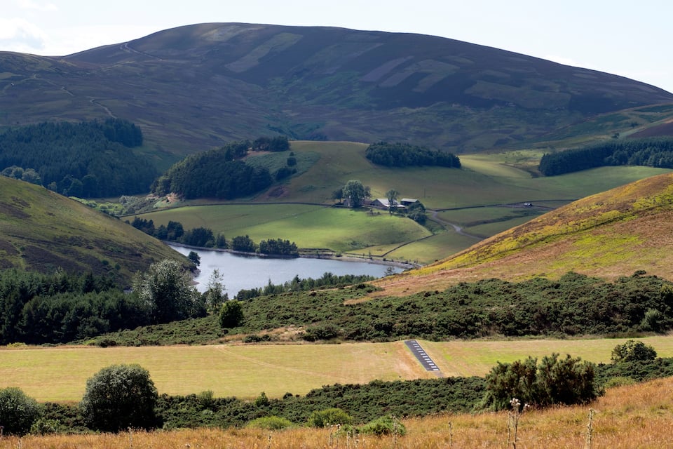 A valley with a lake, rolling hills, and a road.