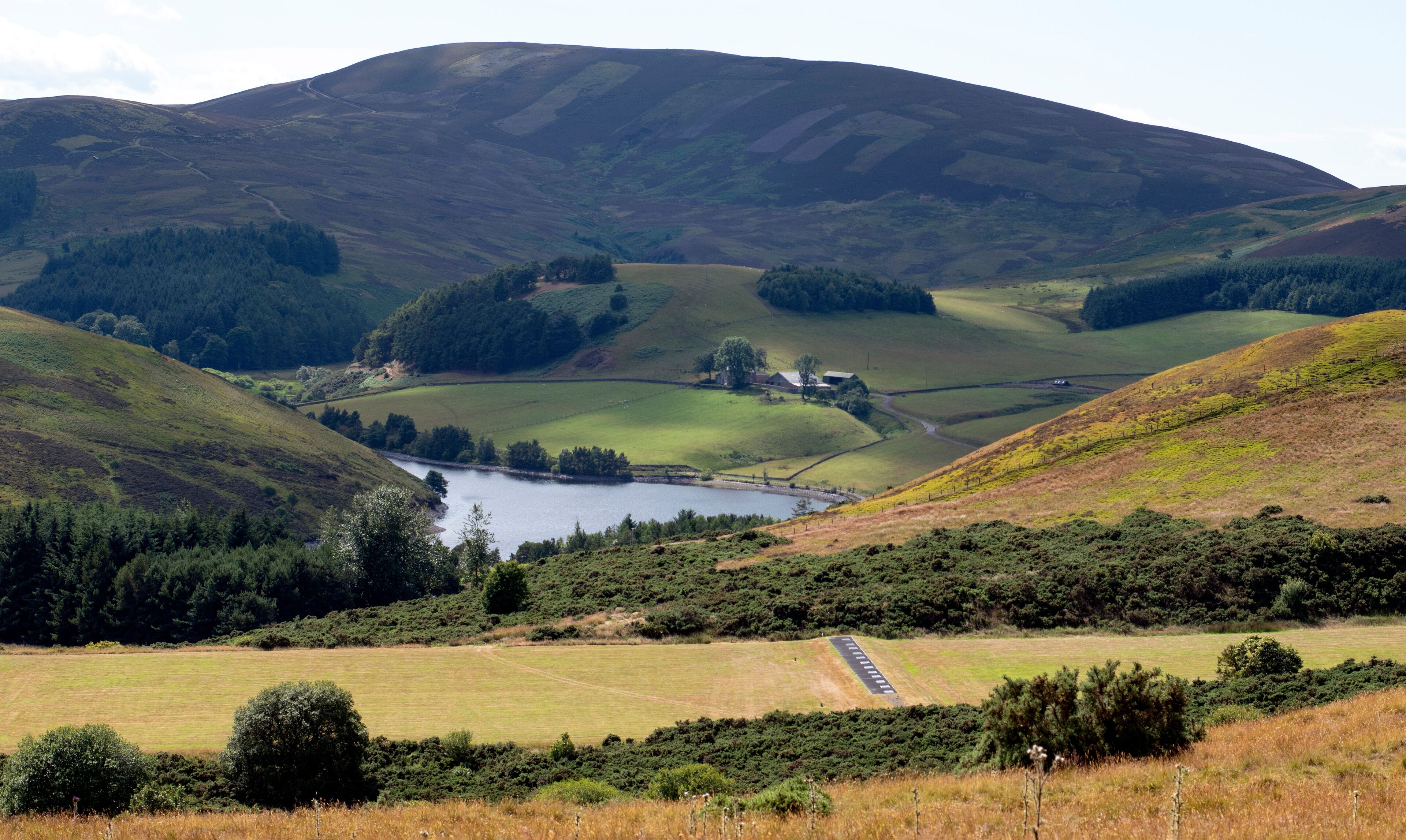 A valley with a lake, rolling hills, and a road.