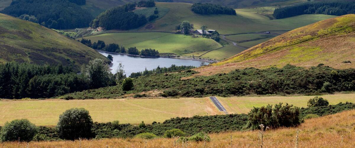 A valley with a lake, rolling hills, and a road.