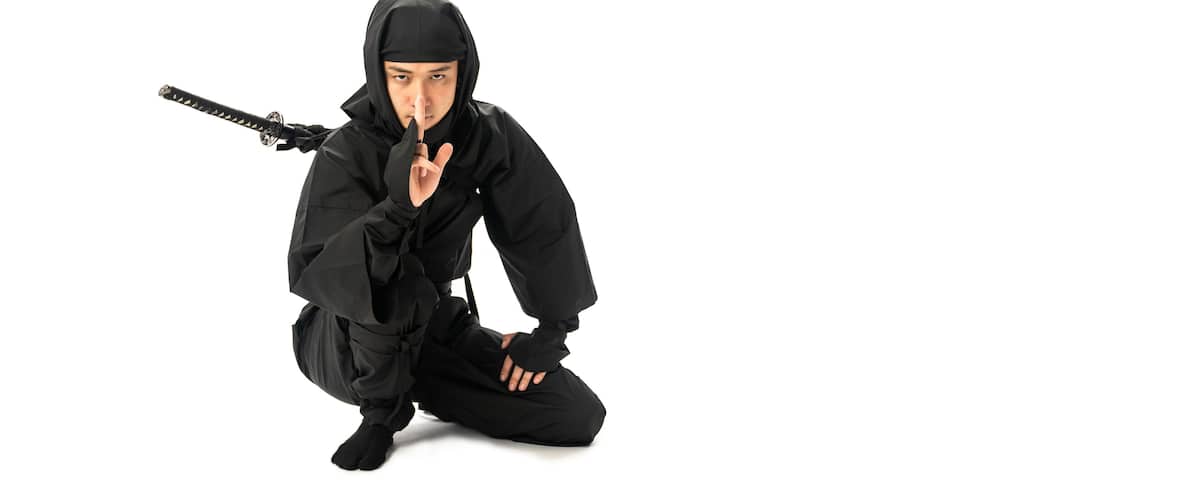 A person in black ninja attire crouching with a sword.