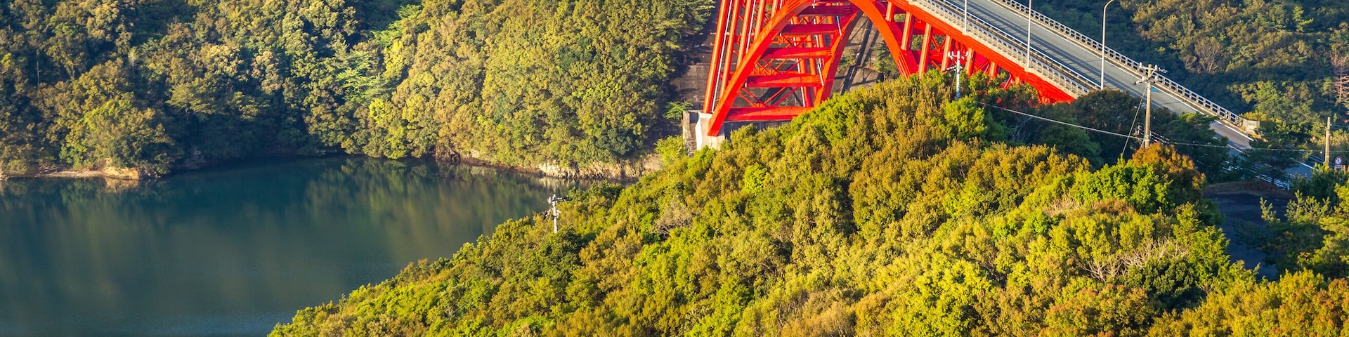 Un puente rojo que cruza un río, rodeado de un bosque denso y colinas.