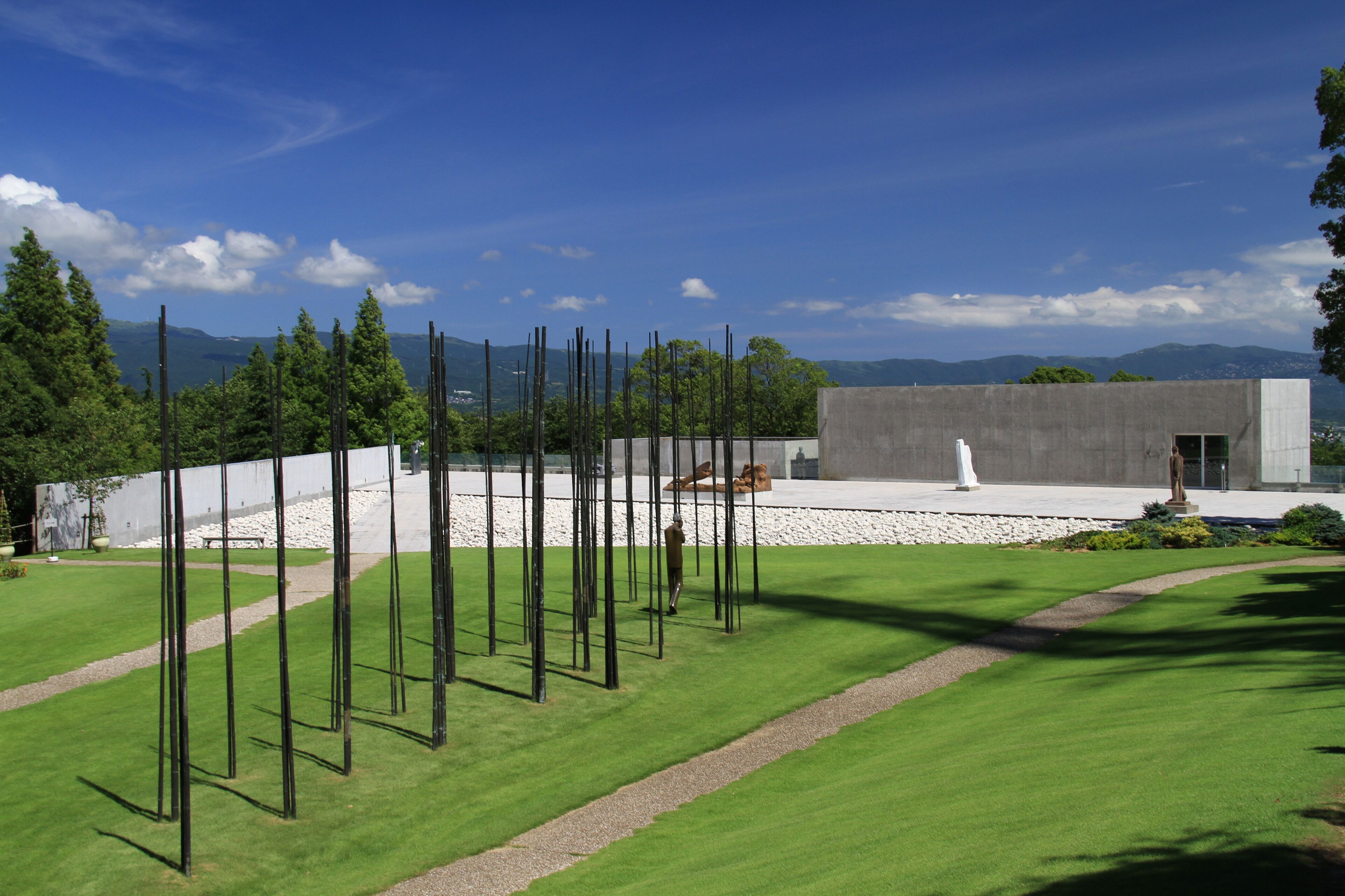 A modern sculpture garden with tall metal poles, a concrete building, and a well-maintained lawn.