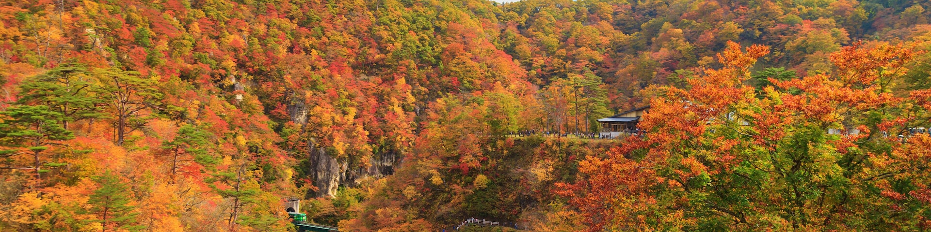 A mountainous landscape with autumn foliage, a winding path, and traditional architecture.
