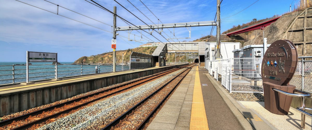 A coastal train station with tracks, platform, and a sign indicating 'Shinagawa'.