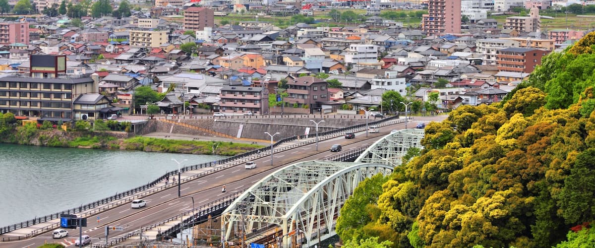 A cityscape with a river, a bridge, and mountains in the background.
