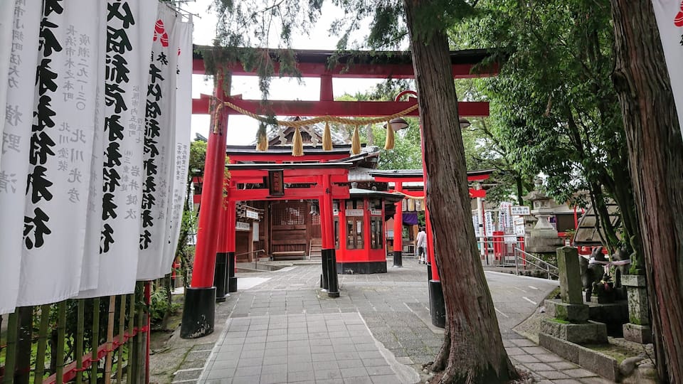 A traditional Japanese torii gate with red pillars and white banners with Japanese characters.