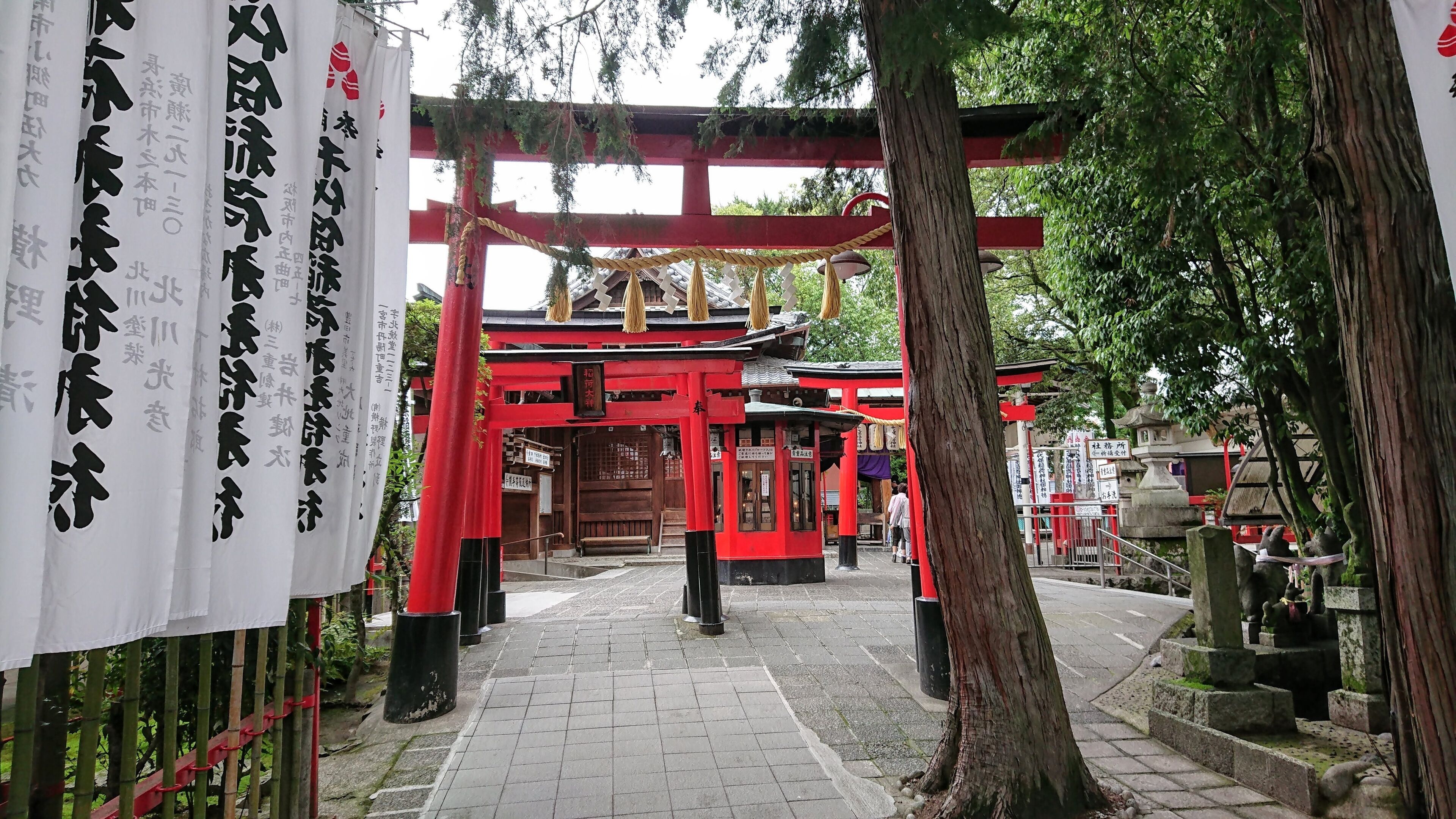 A traditional Japanese torii gate with red pillars and white banners with Japanese characters.