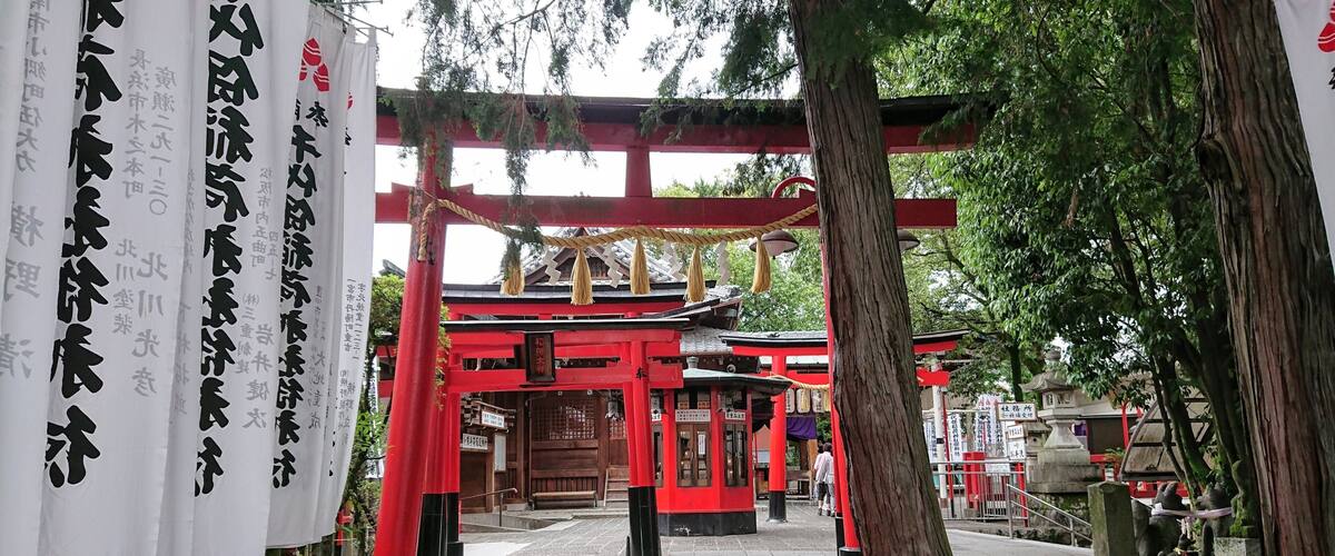 A traditional Japanese torii gate with red pillars and white banners with Japanese characters.