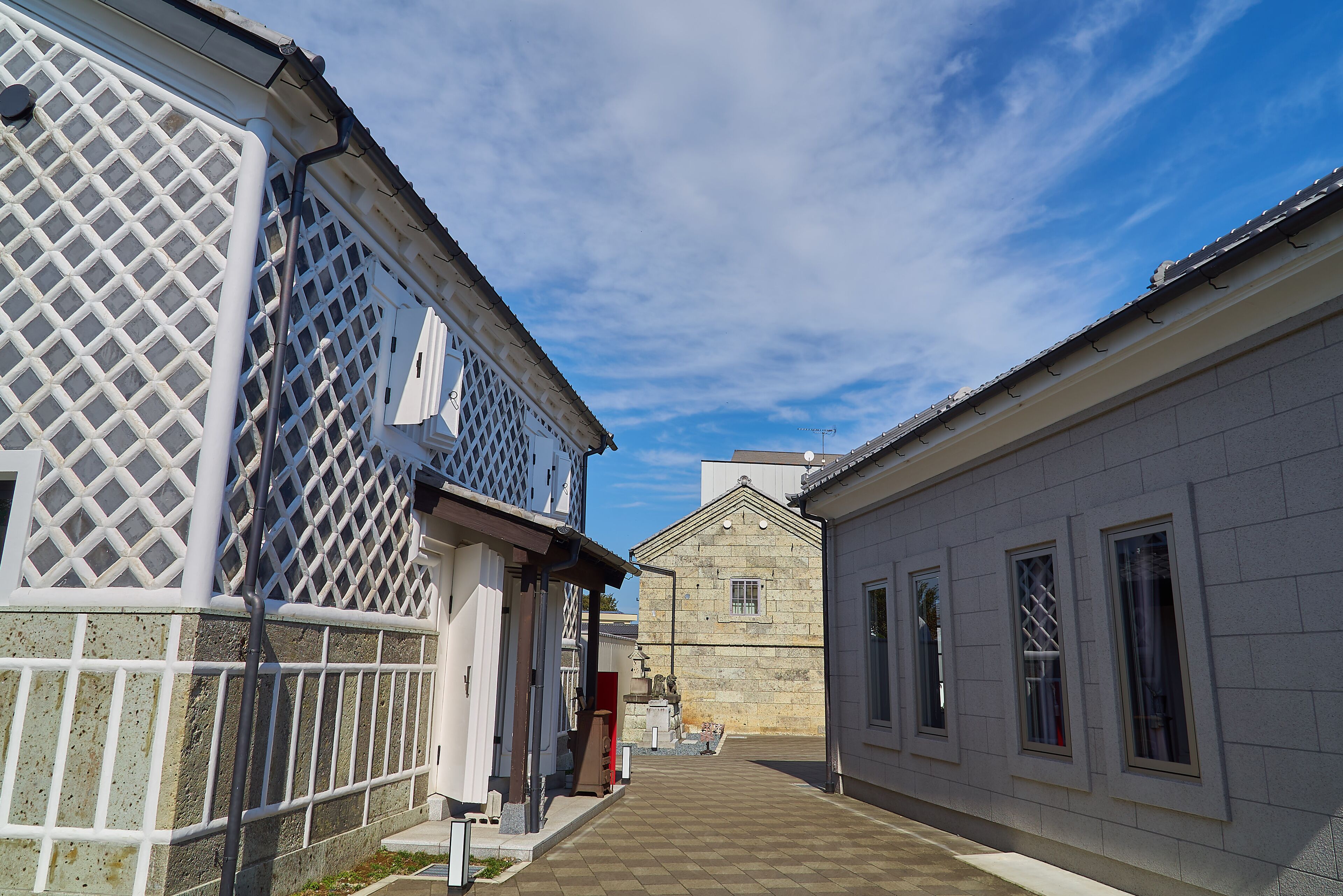 A narrow alley with buildings on either side, featuring lattice windows and a stone building in the distance.