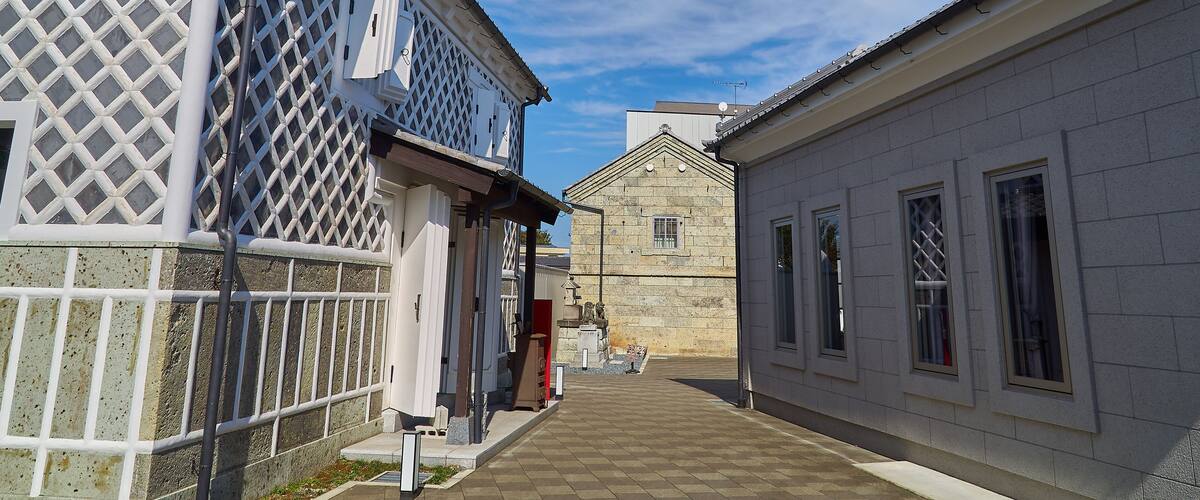 A narrow alley with buildings on either side, featuring lattice windows and a stone building in the distance.
